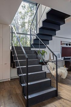 there is a black stair case next to the stairs in this modern living room with wood flooring and white walls