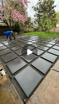 a man is working on an outdoor patio with black tiles and concrete slabs in the foreground