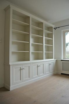 an empty room with white bookcases and wood flooring in front of a window