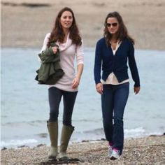 two women walking on the beach next to each other and one is wearing rain boots