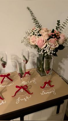 four wine glasses with red bows are sitting on a table next to flowers and greenery