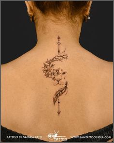 the back of a woman's neck with flowers and arrows tattooed on her left side