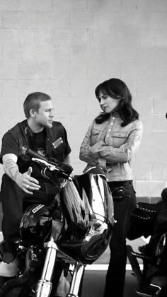 two men and a woman standing next to a motorcycle