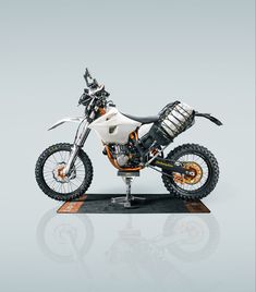 an orange and white dirt bike on a black stand in front of a gray background