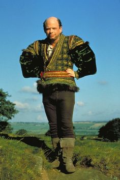 a man standing on top of a lush green field next to a tree covered hillside