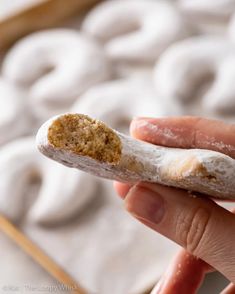 a person holding a piece of food in their hand with doughnuts in the background