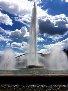 a large fountain spewing water into the air with blue skies and clouds in the background