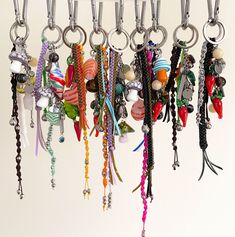 a bunch of key chains hanging from hooks on a white wall with beads and charms attached to them