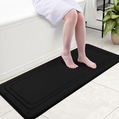 a person standing on a bath mat in a bathroom next to a potted plant