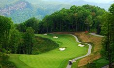 an aerial view of a golf course with green hills in the background and trees on either side