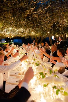 a group of people sitting at a long table with wine glasses in their hands,