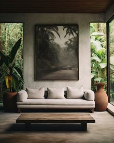 a living room filled with furniture next to a painting and potted plants on the wall