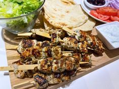 several skewers of meat and vegetables on a cutting board with pita bread