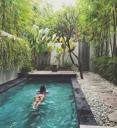 a woman swimming in a small pool surrounded by greenery and stones, with trees