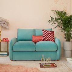 a blue couch sitting in a living room next to a potted plant and rug