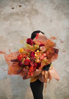 a woman holding a bouquet of flowers in front of a concrete wall with the words autumn written on it