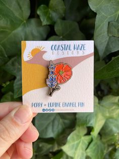 a person holding up a small lapel pin in front of some green leaves and plants