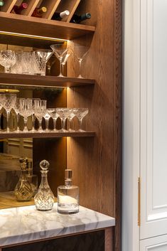 wine glasses and liquor bottles sit on a marble counter in front of a wooden shelf