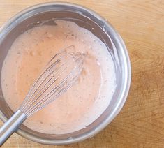 a whisk in a metal bowl on top of a wooden table