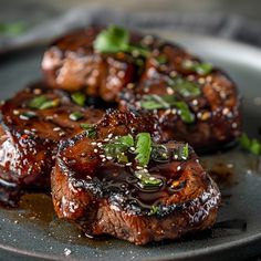 two pieces of meat on a plate covered in sauce and garnished with green leaves