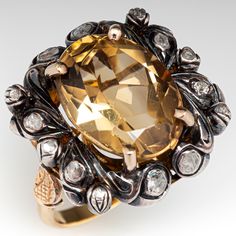 This exquisite circa Victorian era ring is centered with one (1) oval mixed cut natural citrine set into a four-prong setting. The center stone is bordered with fourteen (14) rose cut diamonds that are bead/bezel set into sterling silver settings. The 14K yellow gold under gallery features pierced engraved motifs. The shoulders of the ring features a carved floral design. The ring measures 23.1mm at the top, rises 13.2mm above the finger, tapering to 2.6mm wide and 1.4mm thick at the base of the Luxury Oval Topaz Ring With Gemstone Accents, Luxury Yellow Rings With Rose Cut Diamonds, Victorian Oval Gemstone Diamond Ring, Victorian Oval Diamond Ring With Gemstone, Elegant Oval Multi-stone Topaz Ring, Elegant Multi-stone Citrine Rings, Luxury Yellow Gold Topaz Ring With Rose Cut Diamonds, Elegant Multi-stone Citrine Topaz Ring, Elegant Multi-stone Topaz And Citrine Ring