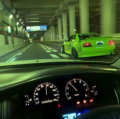 a green car driving down a highway next to tall buildings