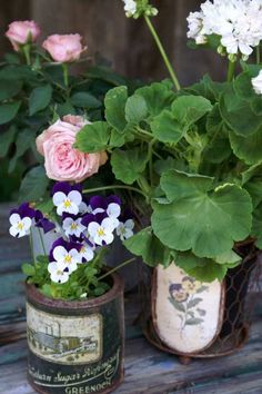 two tin cans filled with flowers sitting on top of a wooden table next to each other