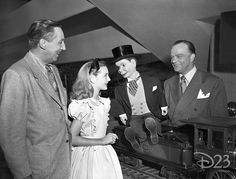 an old black and white photo of three people talking to one another while the other man is wearing a top hat