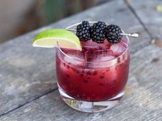 a drink with blackberries and lime garnish sits on a wooden table