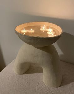 there is a bowl with candles in it on top of a white tableclothed surface