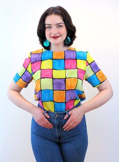 "This is a sweet colorful 90s vintage \"Notations\" top! It's a bright color block geometric square print in shades of pink, blue, yellow, purple and orange with black grid lines. A short sleeved pullover, it has a boxy shape, a high round neckline, no shoulder pads, and it closes with a back keyhole neckline and a black button and loop. The fabric is a lightweight silken polyester. This top is in very good clean vintage condition, no flaws noted. The label says \"Notations, Size S, 100% Polyest Retro Multicolor Tops With Rainbow Print, Retro Multicolor Rainbow Print Top, Retro Multicolor Top With Geometric Pattern, Fitted Retro Multicolor Tops, Retro Blue Top With Colorful Pattern, Retro Multicolor Tops With Retro Print, Multicolor Retro Print Tops, Retro Plaid Top With Graphic Print, Colorful Retro Color Block Tops