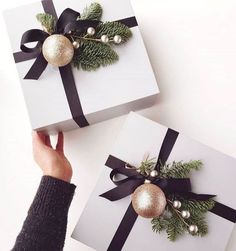 two presents wrapped in white paper with black ribbon and gold ornaments on them, being held by someone's hand