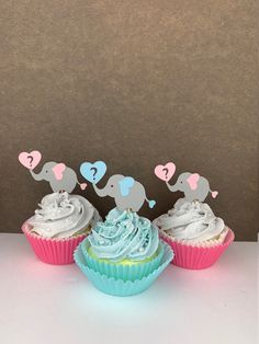 three cupcakes with white frosting and blue icing, on a table