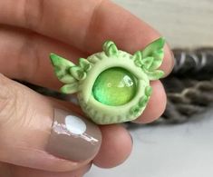 a hand holding a tiny green ring with leaves on it's center and an eyeball in the middle