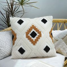 a white and orange pillow sitting on top of a bed next to a plant in a vase