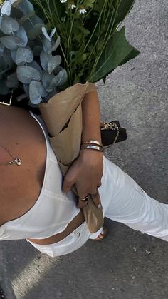 a woman carrying a bouquet of flowers on her back while walking down the street in white pants