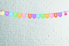 a happy birthday banner hanging from a string on a white brick wall with the words happy birthday written across it