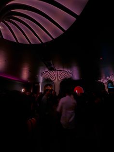 a group of people standing around in a dark room with lights on the ceiling and columns