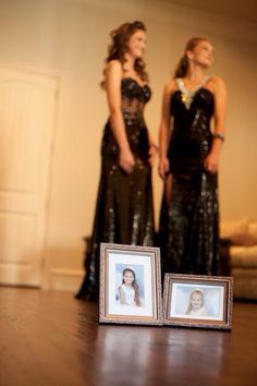 two women in black dresses standing next to each other with pictures on the floor behind them