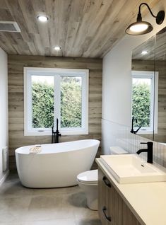 a white bath tub sitting next to a window in a bathroom under wooden ceilinging