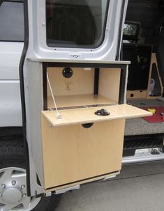 a small wooden cabinet in the back of a van with its door open and wheels out