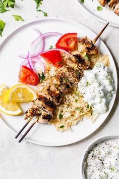 grilled chicken and rice on a white plate with lemon wedges, tomatoes, onions, and garnishes