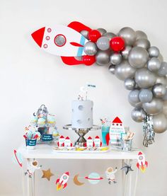 a space themed birthday party with silver balloons and rocket ship decorations on a white table