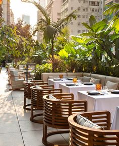 an outdoor dining area with tables, chairs and plants on the side walk in front of tall buildings