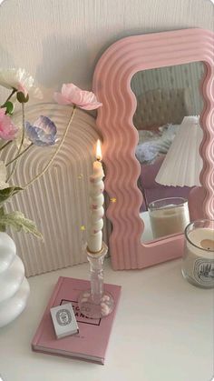 a white table topped with a pink mirror next to a vase filled with flowers and candles