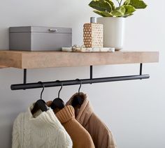 two sweaters are hanging on a shelf next to a potted plant