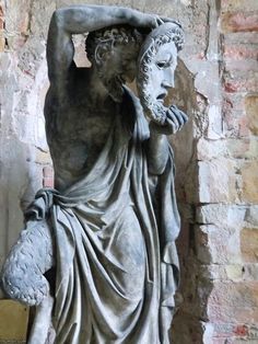 a statue is shown in front of a brick wall and stone pillars, with one person covering his face