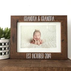 a wooden frame with a baby's photo in it on a shelf next to a potted plant