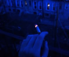 a hand holding a lit up bottle in front of a building at night with the light on