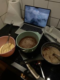 a laptop computer sitting on top of a counter next to bowls and whisks